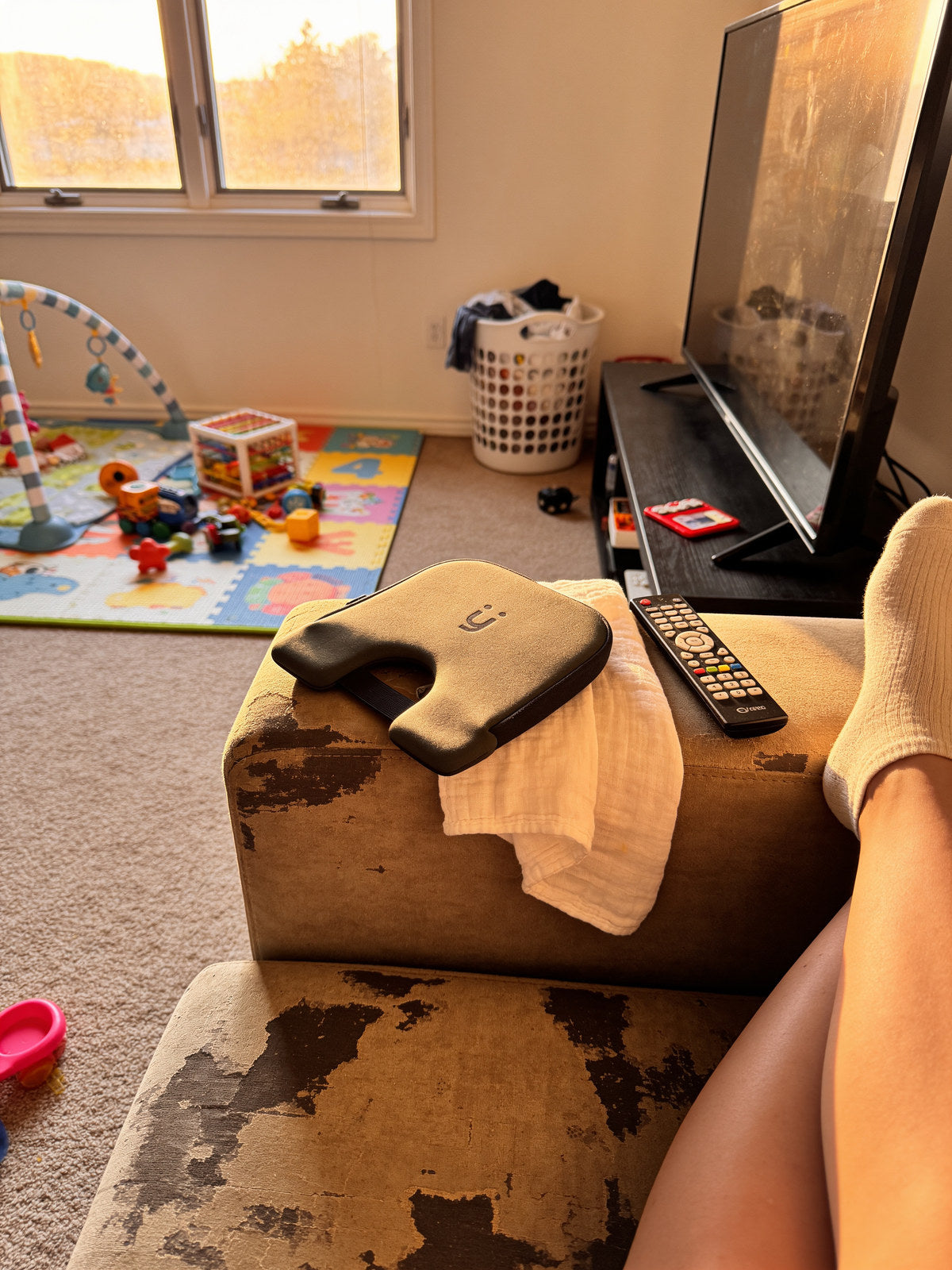 The Babi Seat cushion on a sofa arm with toys on the rug behind